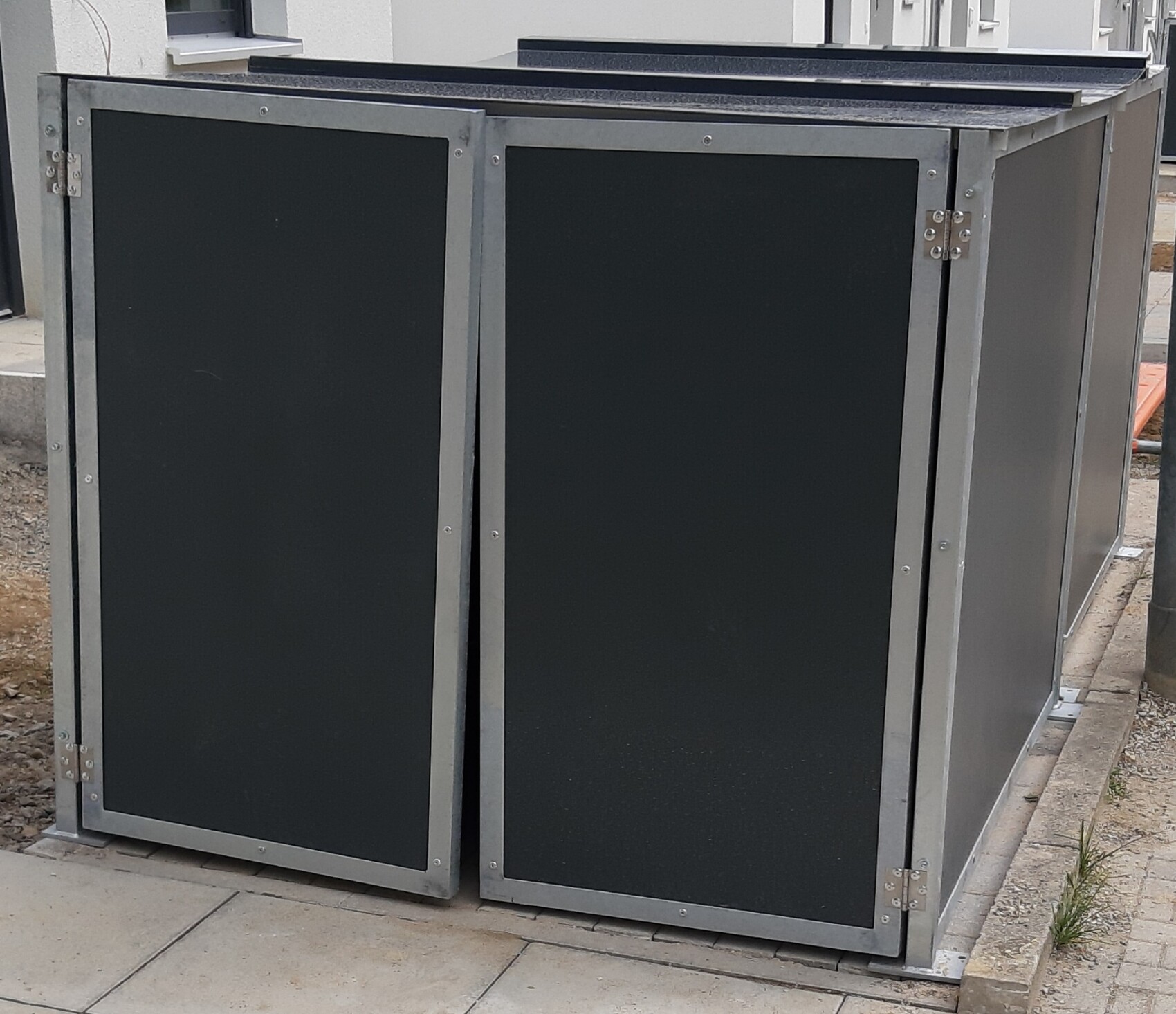 Zwei große schwarze Transportkisten mit silbernem Metallrahmen stehen draußen auf Betonplatten.