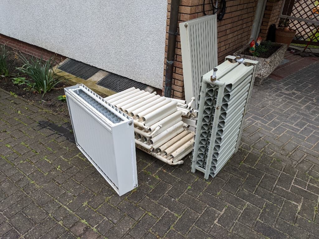 Gebrauchte Heizkörper und Rohre stapeln sich auf dem gepflasterten Hof.
