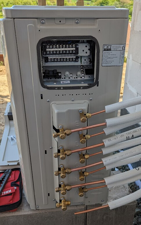 Außeneinheit einer Klimaanlage mit offener Elektrik und mehreren Kupferrohren inkl. Isolierung.