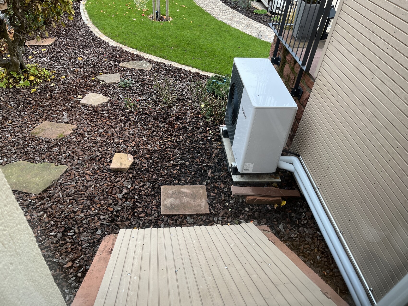 Außen-Klimagerät einer Klimaanlage neben der Hauswand auf Kiesboden im Garten.