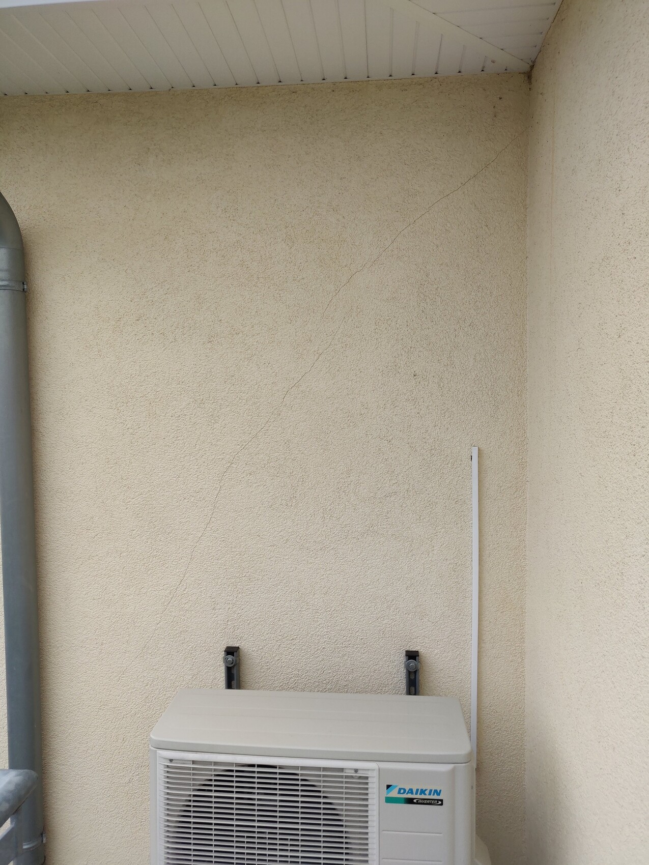 Außengerät einer Daikin-Klimaanlage vor beige verputzte Wand unter dem Vordach