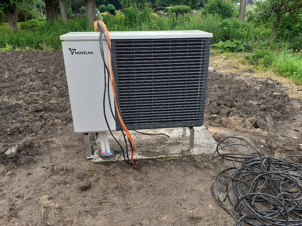 Außeneinheit einer Klimaanlage (Kondensator) mit NOVELAN-Logo auf Betonfundament; Kabel daneben.