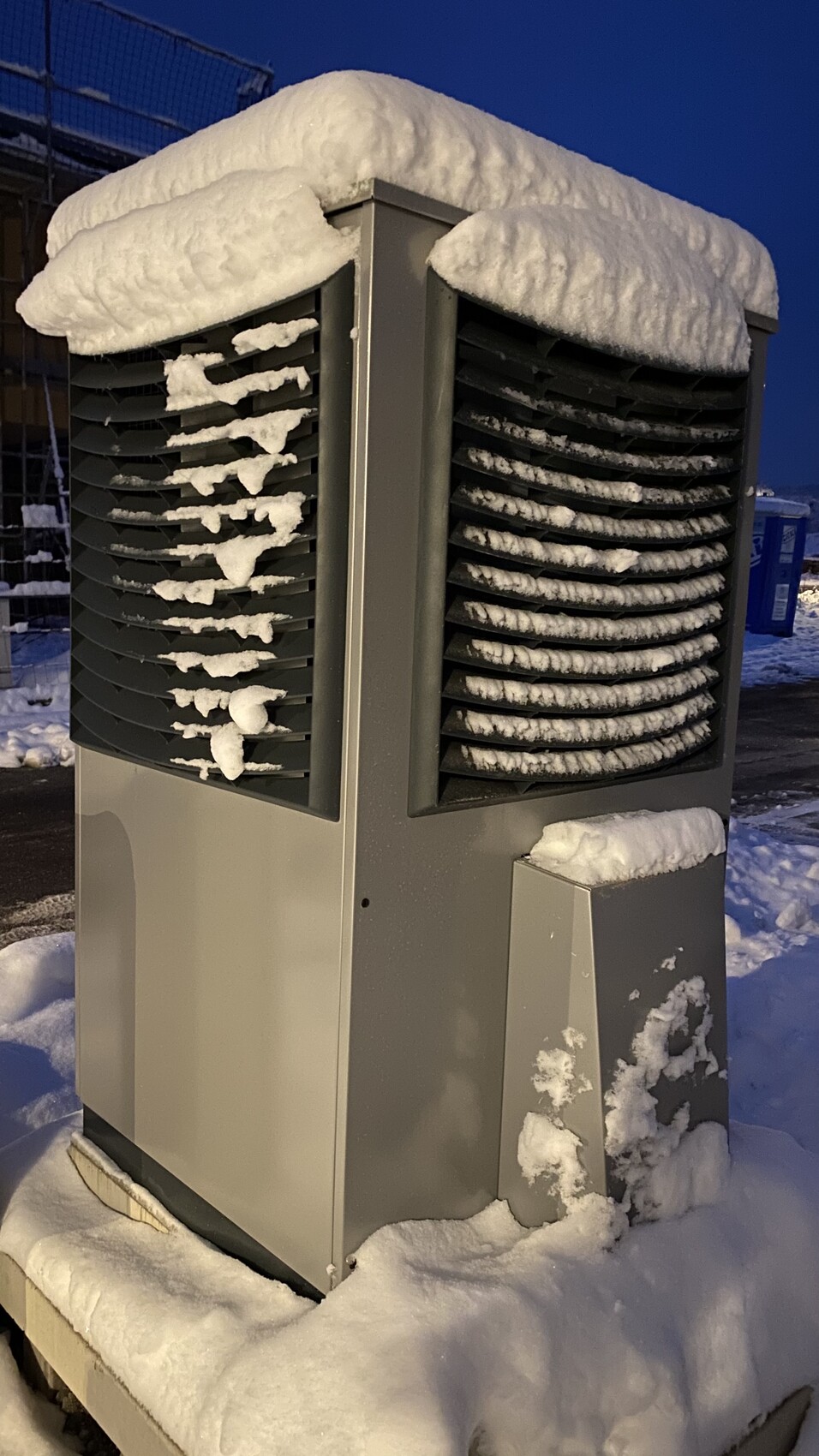 Außen-AC-Einheit im Schnee mit Schneeschicht auf den Lamellen bei Nacht