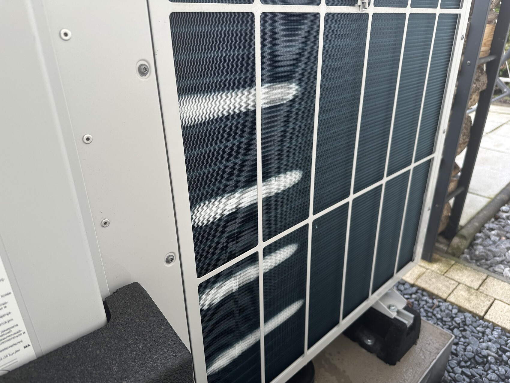 Außenkondensator einer Klimaanlage mit Metallgitter, auf Betonfundament installiert.