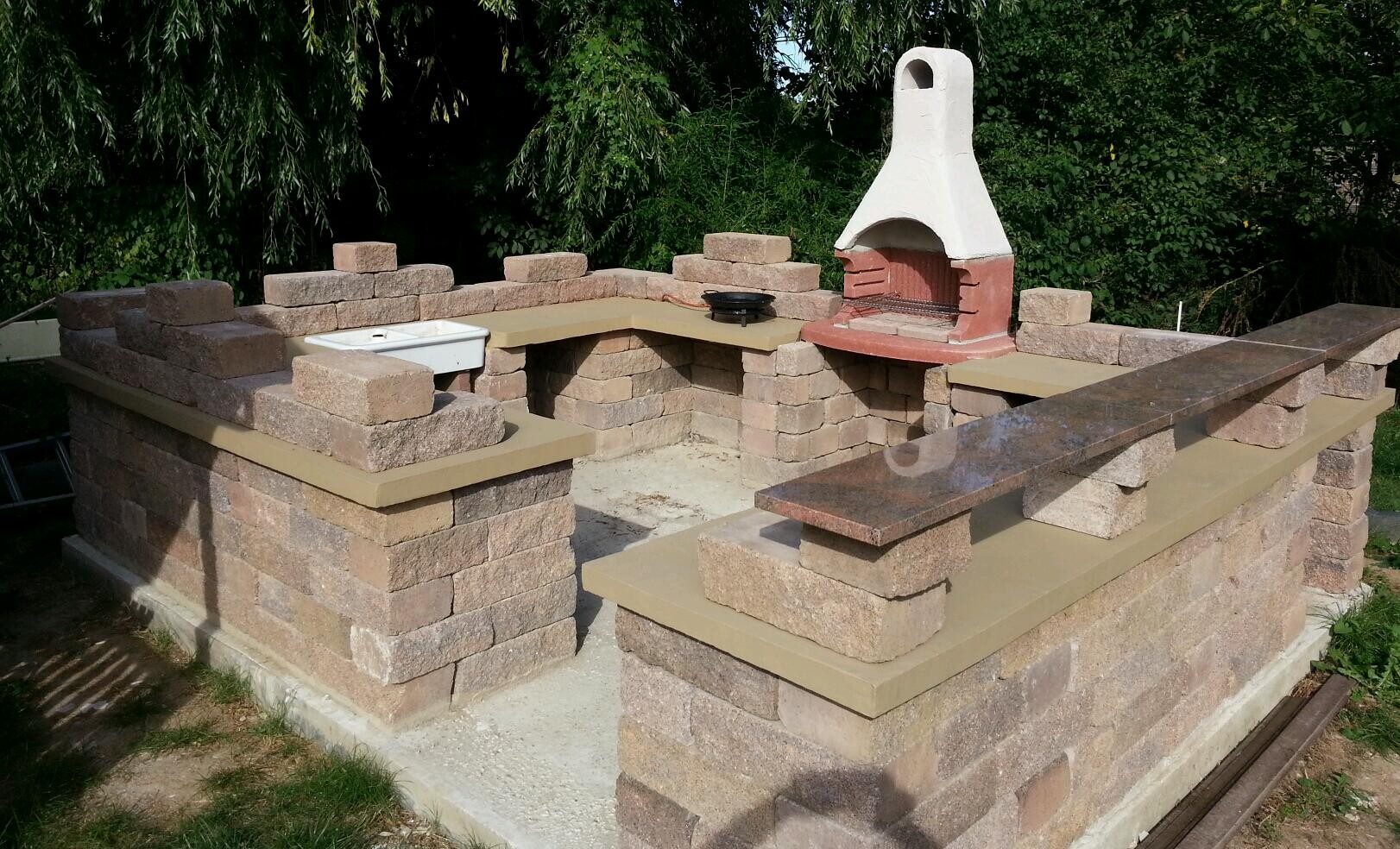 Außenküche aus Stein mit Grill, Steinwänden, Spüle und Arbeitsplatten im Garten.