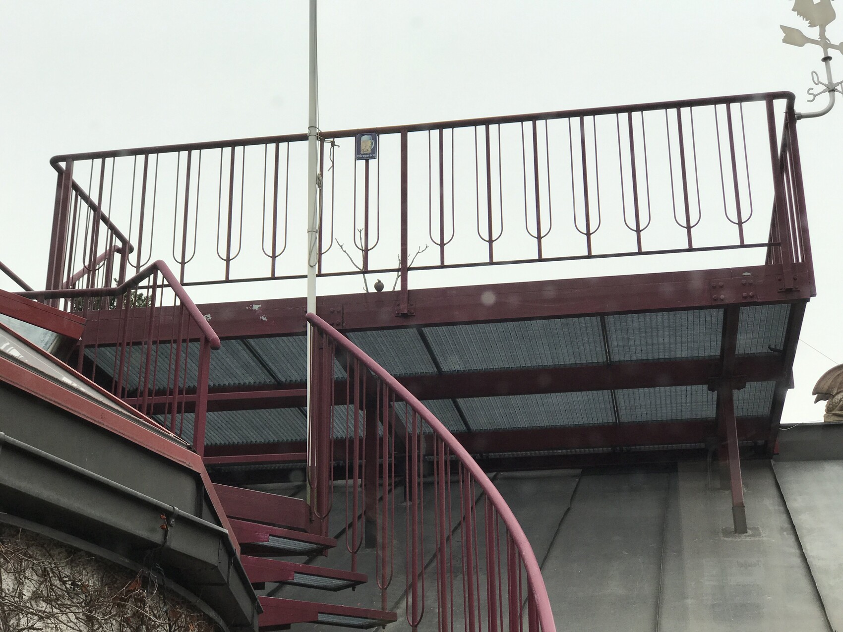 Rote Metalltreppe führt zu einem Balkon mit Geländer über grauem Gebäude.