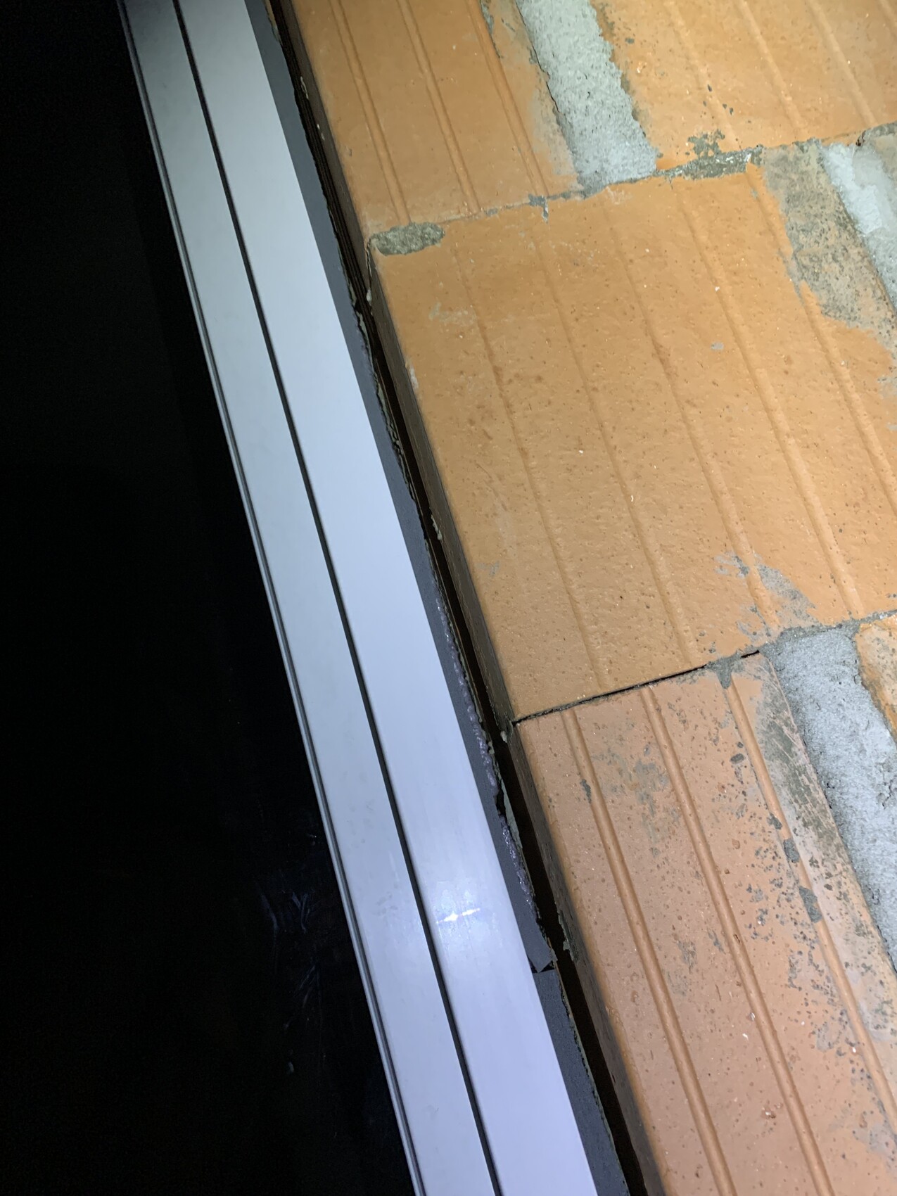 Türzarge aus Aluminium neben einer Ziegelwand; Übergang zwischen Innenraum und Außenbereich.