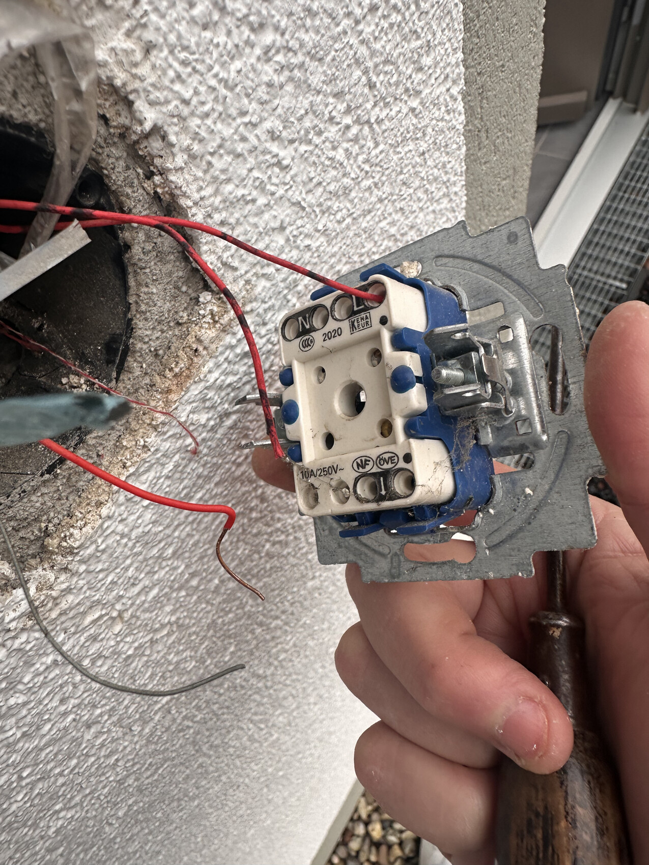 Außenwand: Schalter/Steckdosen-Modul mit freiliegenden Kabeln, Hand mit Schraubendreher