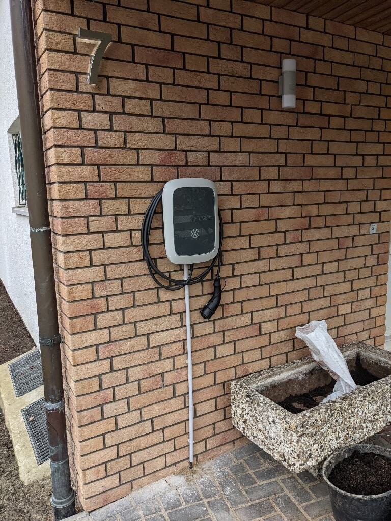 Außen-Ladestation für Elektroauto an Ziegelwand, Kabel um Halterung, Stecker hängt.