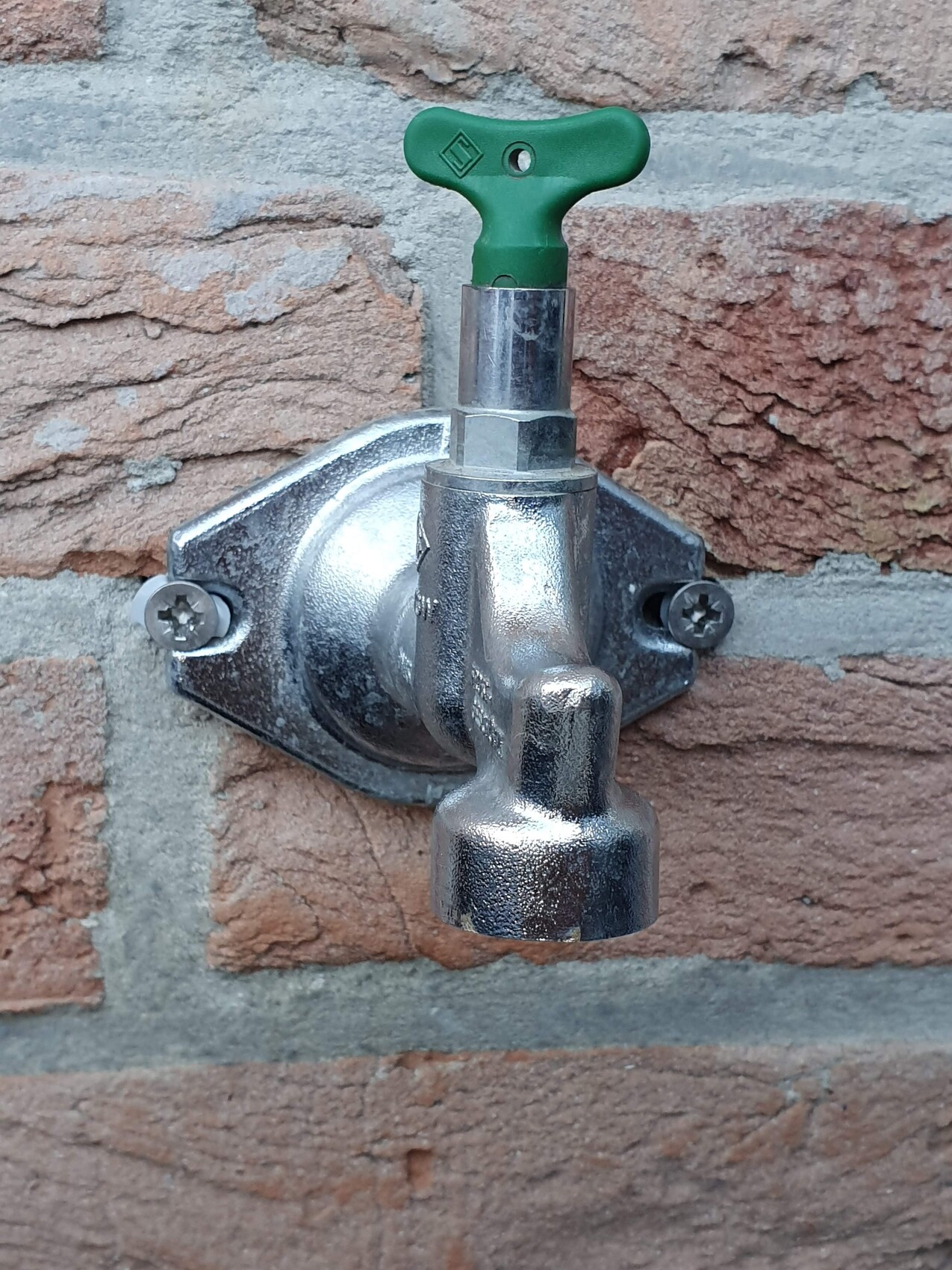 Außen-Wasserhahn aus Metall mit grünem Griff an roter Ziegelwand