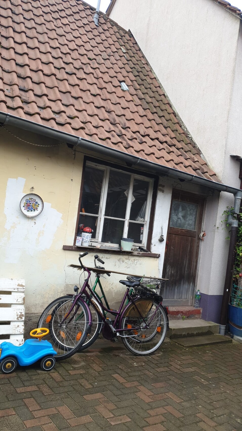 Vorderansicht eines Hauses mit rotem Ziegeldach, Fenster und Tür; davor stehen zwei Fahrräder.