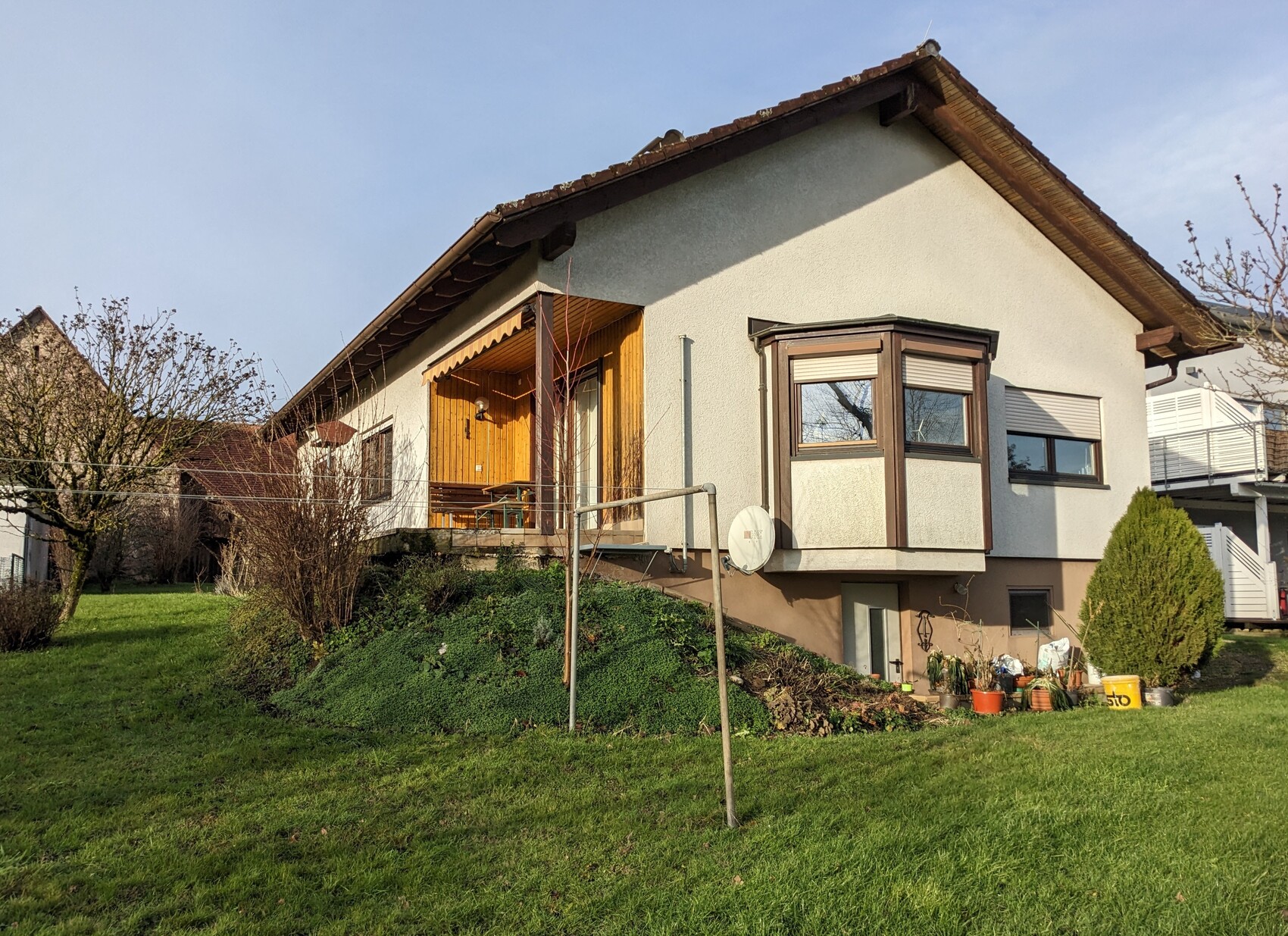 Einfamilienhaus mit Satteldach, Holzveranda, Satellitenschüssel und Garten.