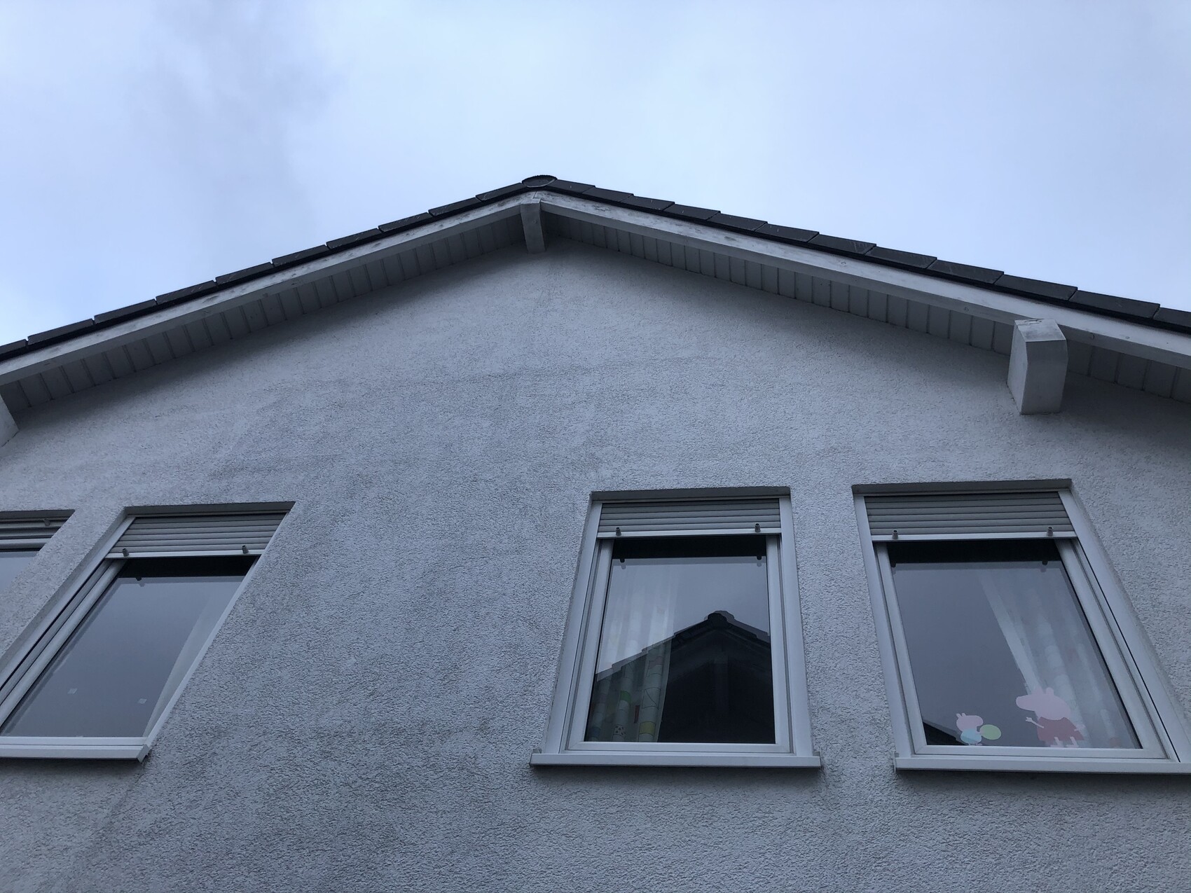 Außenansicht eines grauen Hauses von unten; drei Fenster unter dem Dach, blauer Himmel
