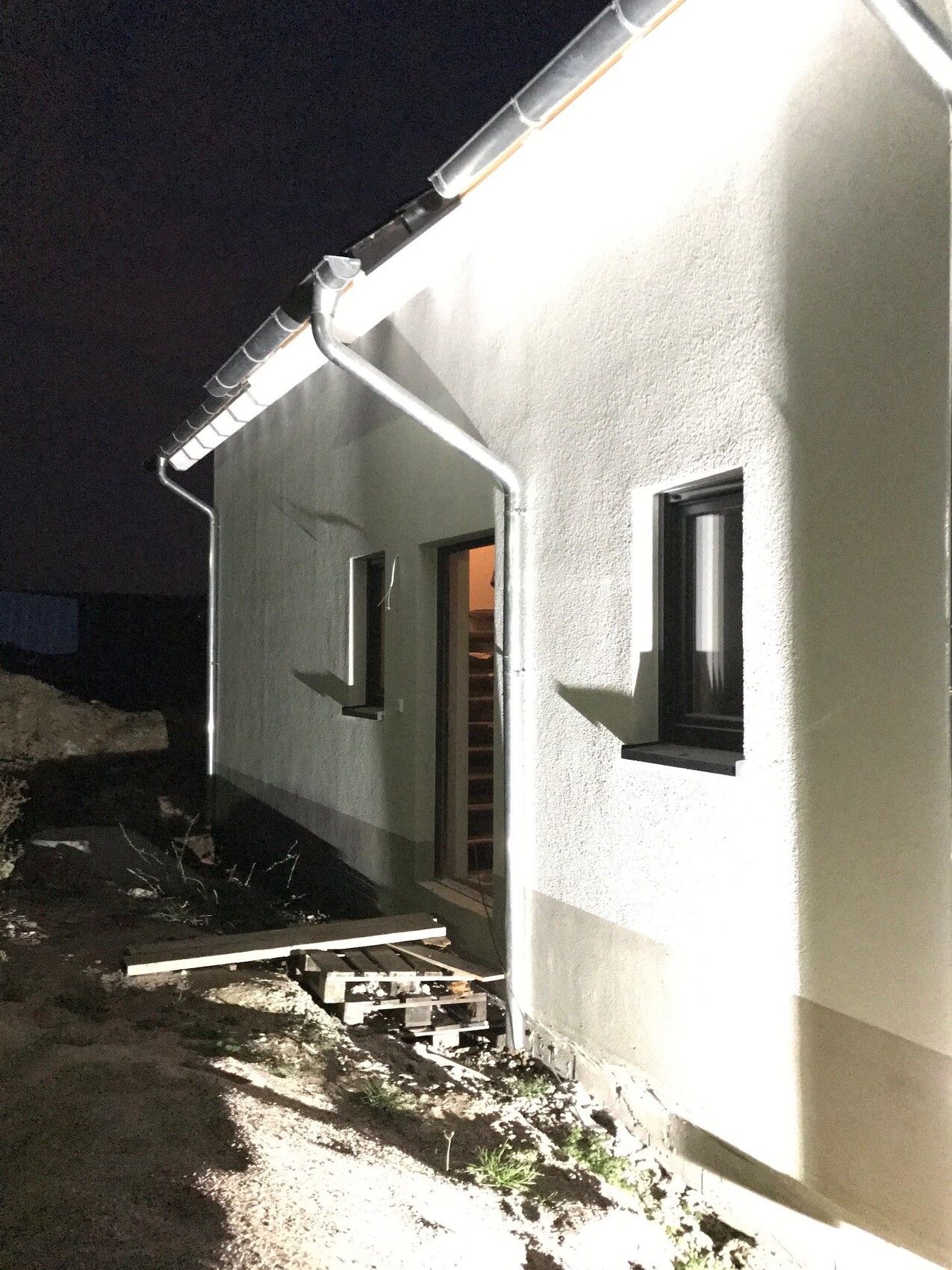 Außenansicht eines Hauses bei Nacht mit Tür, Fenstern und Dachrinne