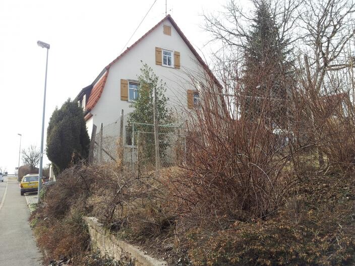 Außenansicht eines Einfamilienhauses am Straßenrand mit Büschen und Zäunen
