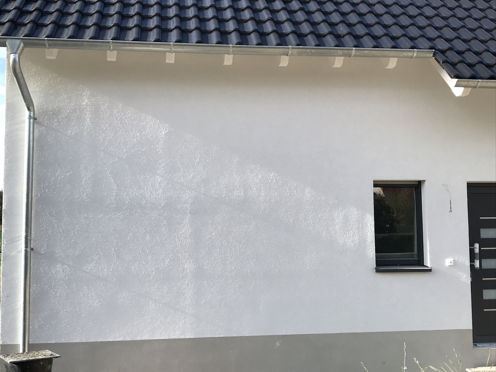 Außenansicht einer Hauswand mit Fenster und Tür, Dachrinne sichtbar