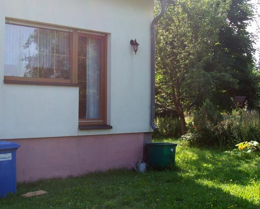Außenansicht eines Hauses mit Fenster, Laterne, Garten und Muelltonnen im Vordergrund.