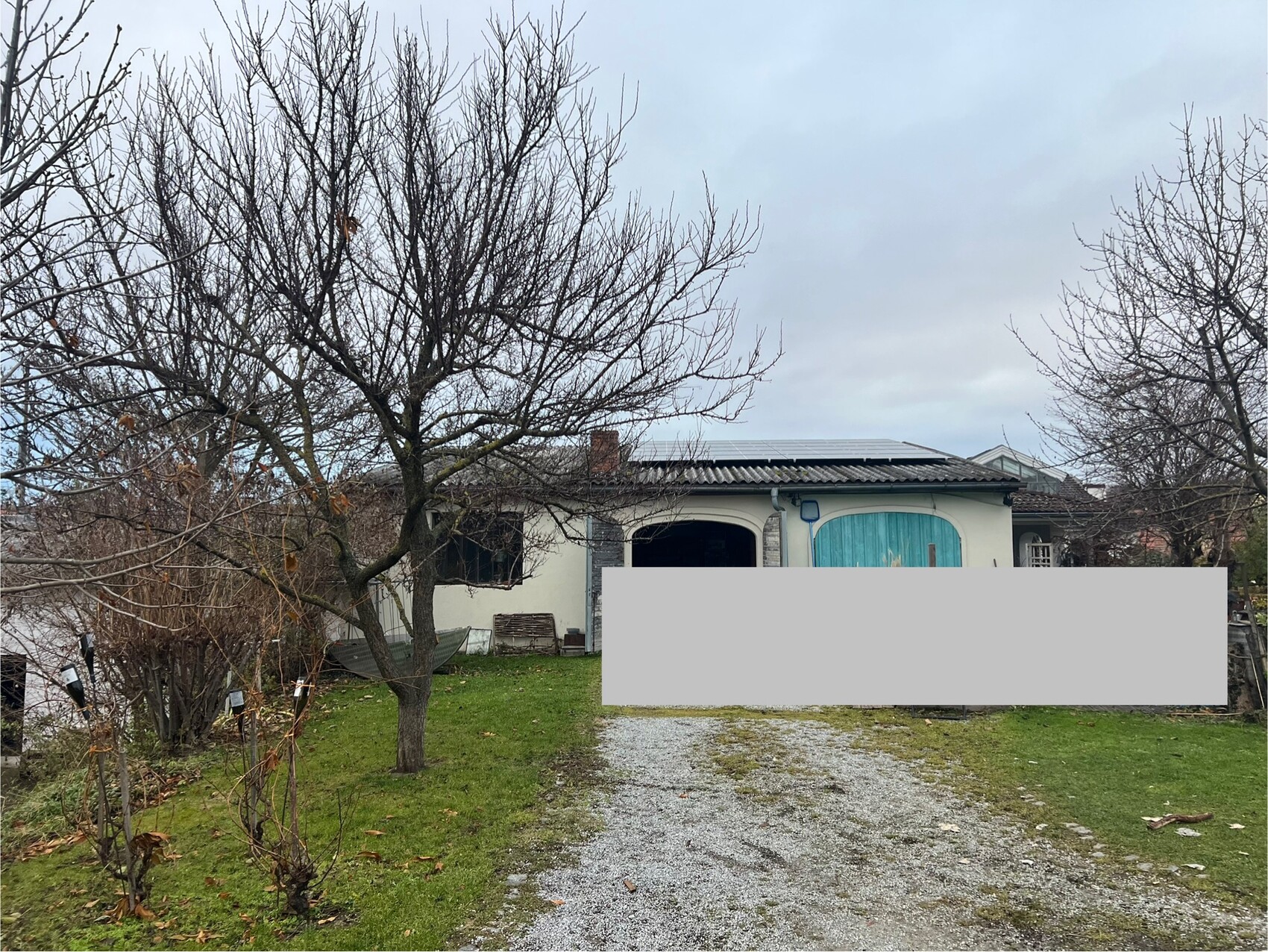 Einfamilienhaus mit Vorgarten, kahle Bäume, Kiesweg zur Eingangstür.