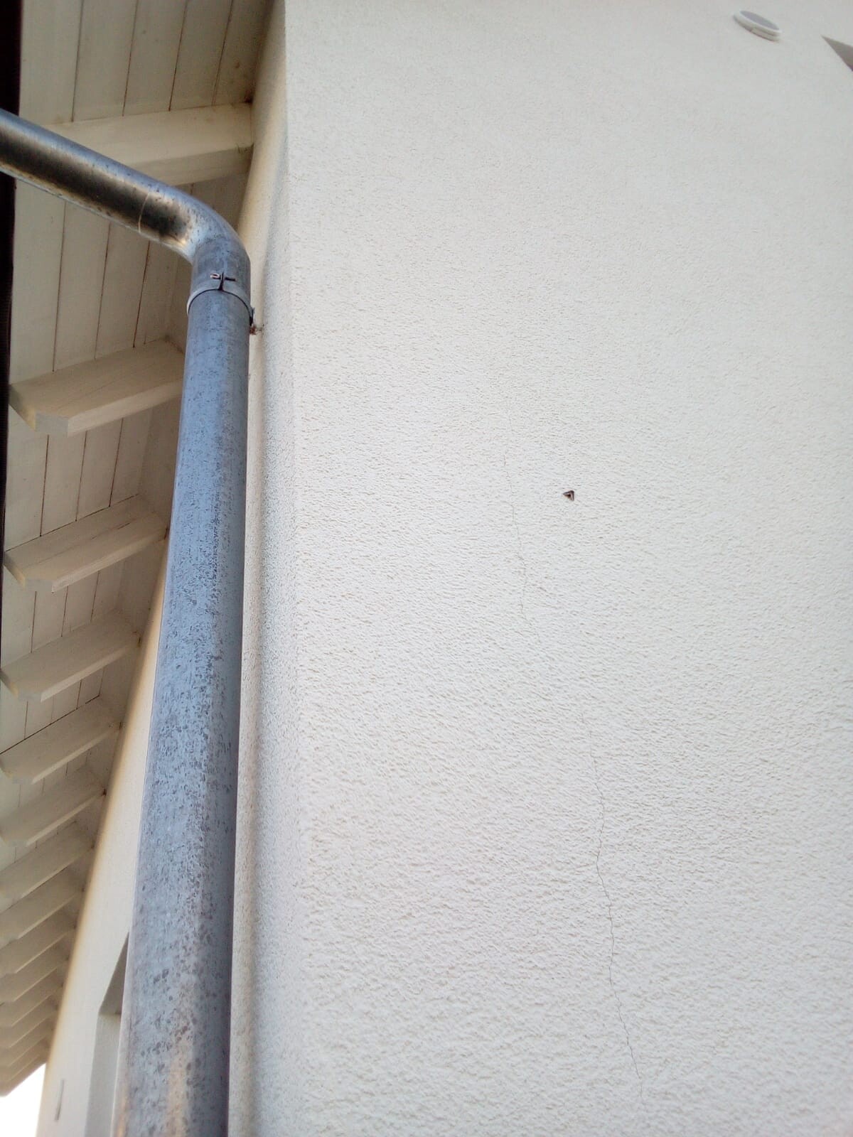 Außenansicht eines Hauses: blaues Fallrohr neben Holztreppe und verputzter Wand