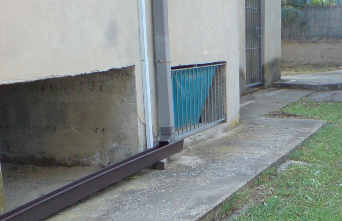 Außenansicht eines Gebäudes mit Fundamentmauer, Geländer und Betonweg