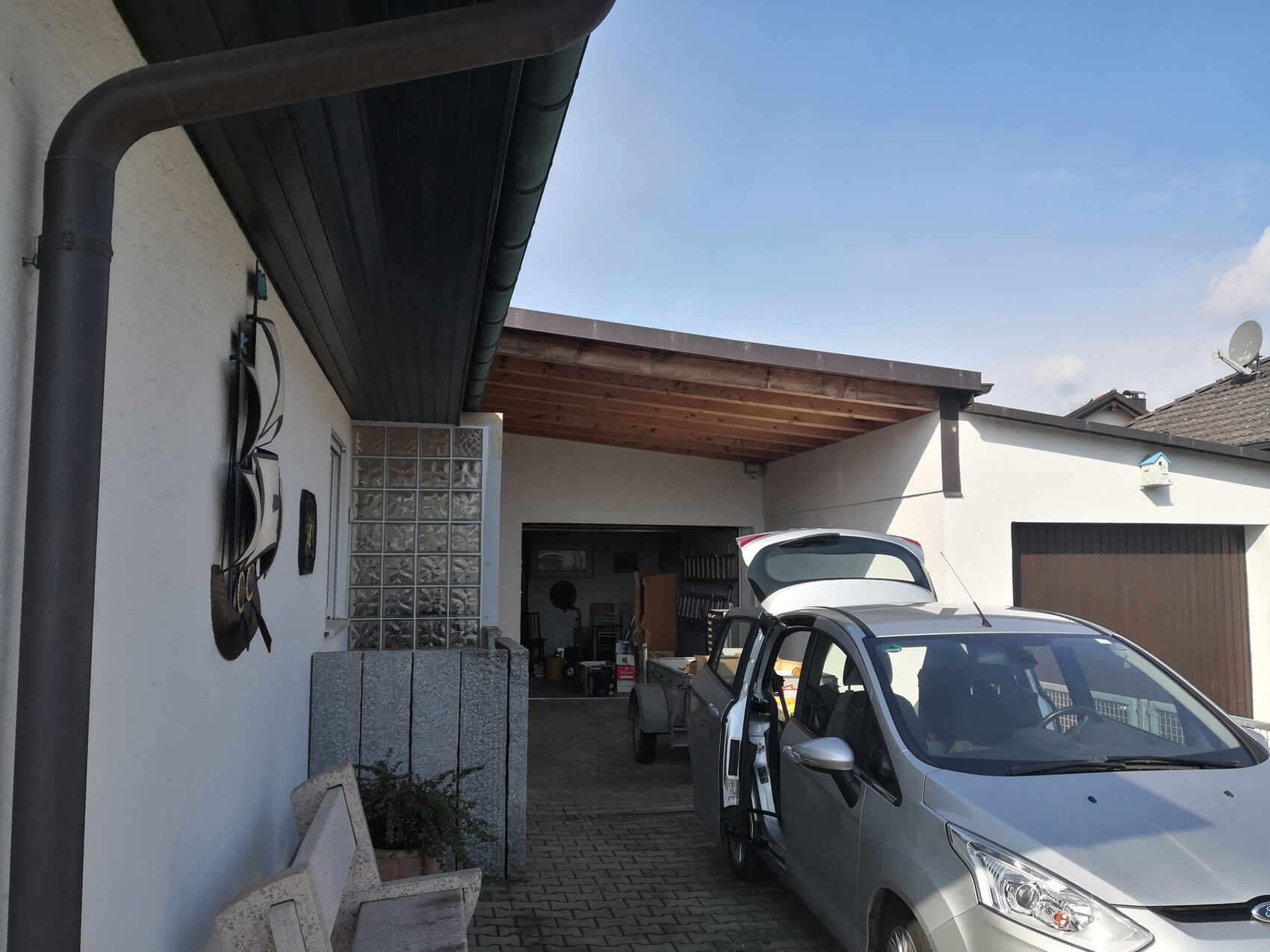 Silberner Van mit geöffneter Heckklappe am Carport, davor Hof mit Werkzeugen.