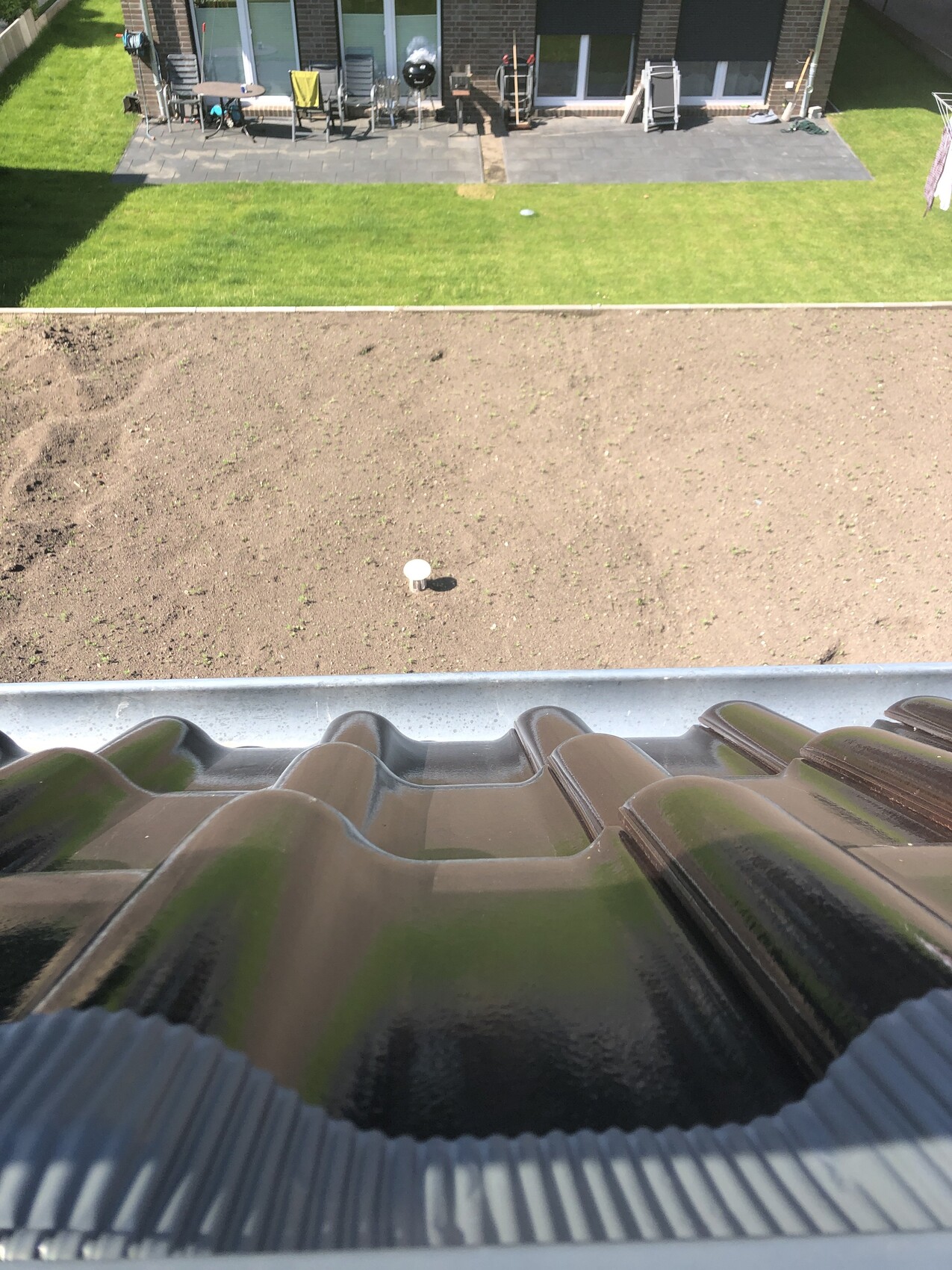 Blick vom Dach auf einen Garten mit brachliegendem Boden, grünem Rasen und Terrassenmöbeln.