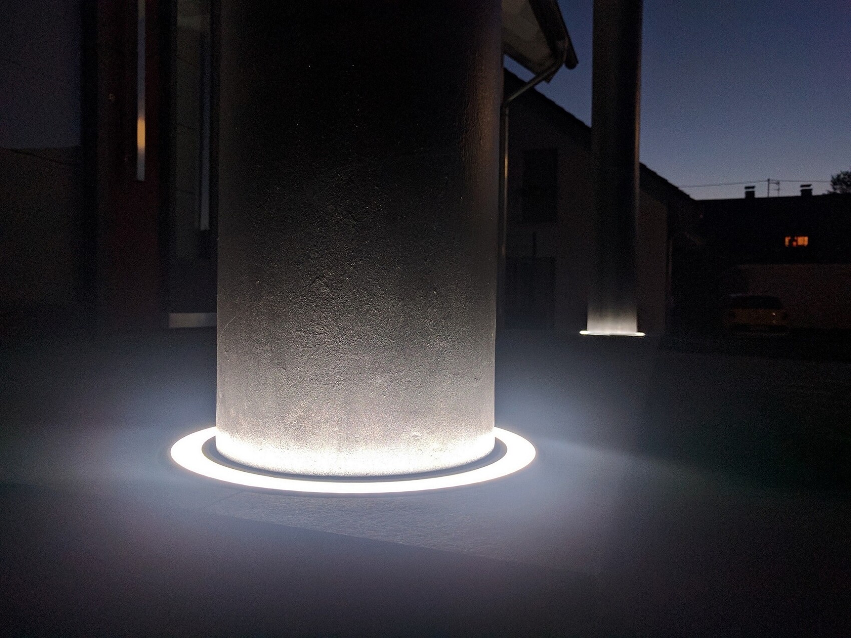 Nächtliche Außenbeleuchtung: Steinpfosten mit hellem Lichtkreis am Boden.