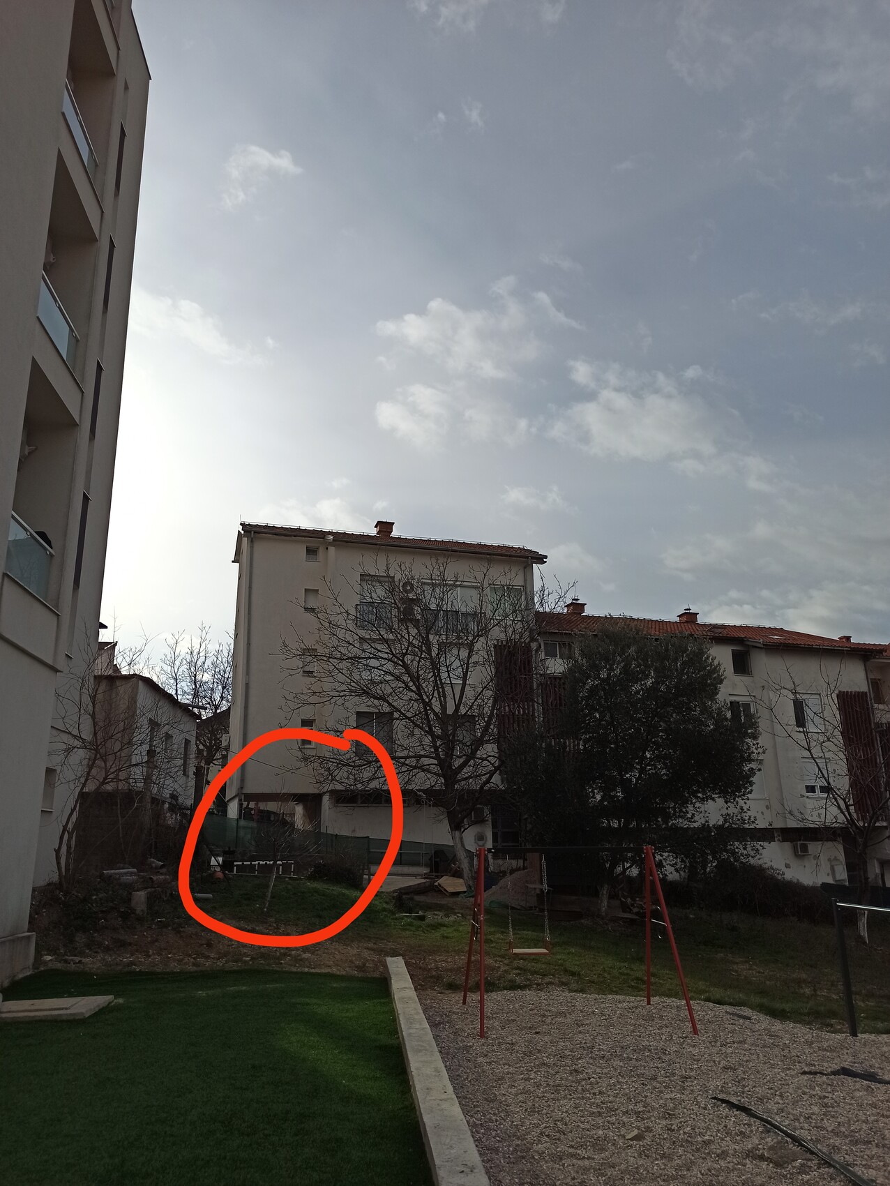 Wohnhof mit Spielplatz, Bäumen und mehrstöckigen Häusern; roter Kreis markiert einen Bereich.
