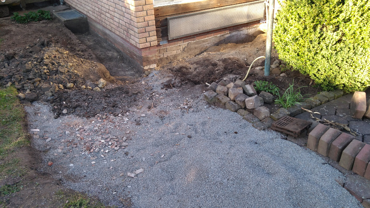 Außenbereich am Haus: Kies, Erdreich, Steine, Pflaster und Drainagegitter.