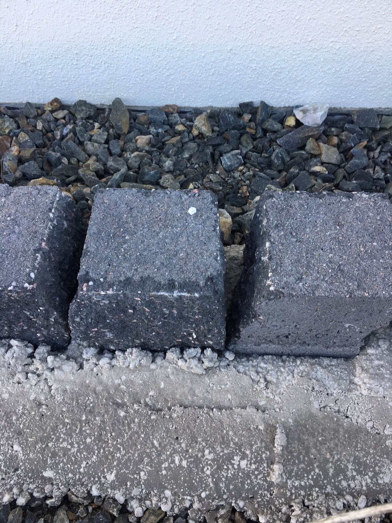 Außenbereich mit Pflastersteinen vor weißer Wand und Kies dahinter.