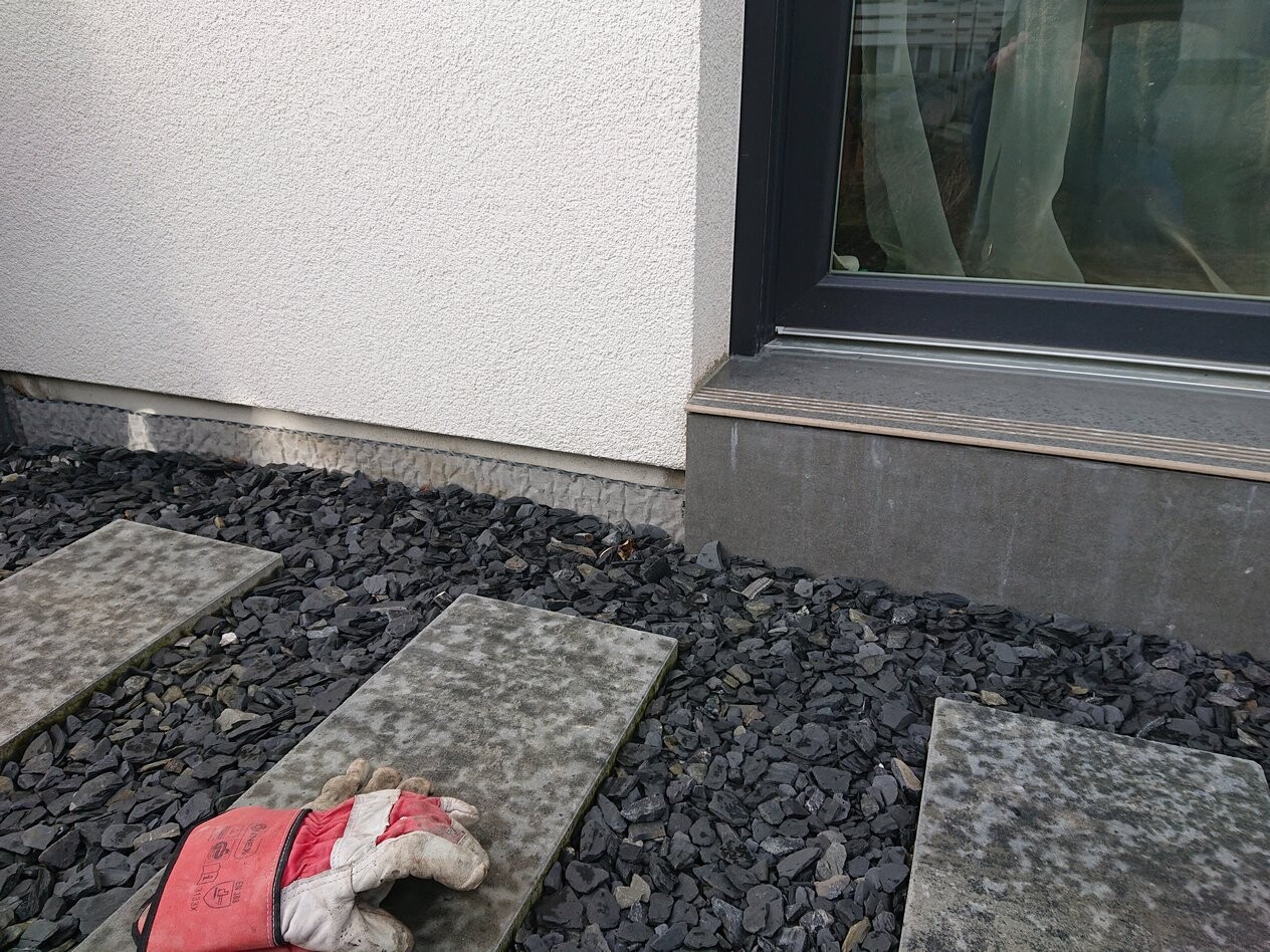 Außenbereich: Kiesweg mit Betonplatten, rote Handschuhe liegen auf einer Steinplatte vor dem Fenster.