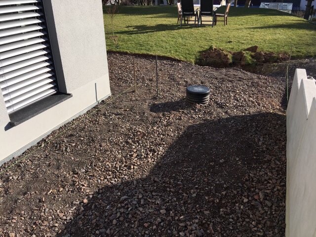 Kiesboden am Haus, runde Belüftung, Grasgarten mit Gartentisch und Stühle im Hintergrund.