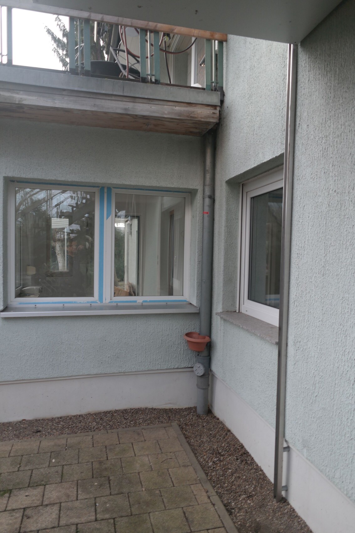 Außenansicht eines Gebäudes mit Eckfenster, Regenrohr und kleinem Blumentopf am Rohr.