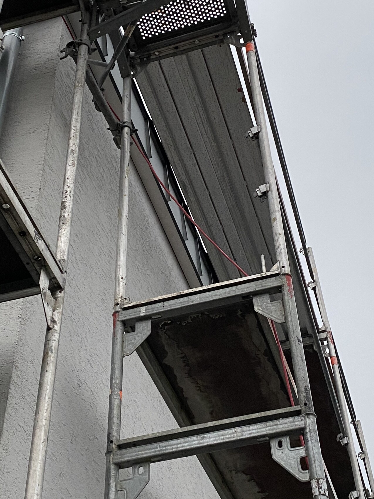 Metallgerüst vor einer Gebäudewand mit Plattform, Geländer und Rohren.