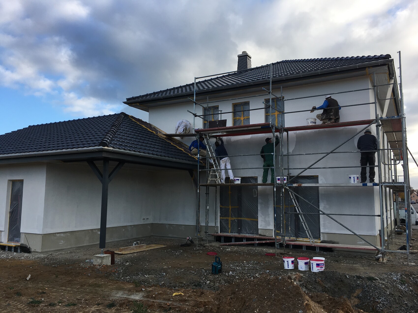 Bauarbeiter streichen die Außenfassade eines zweistöckigen Hauses mit Gerüst.