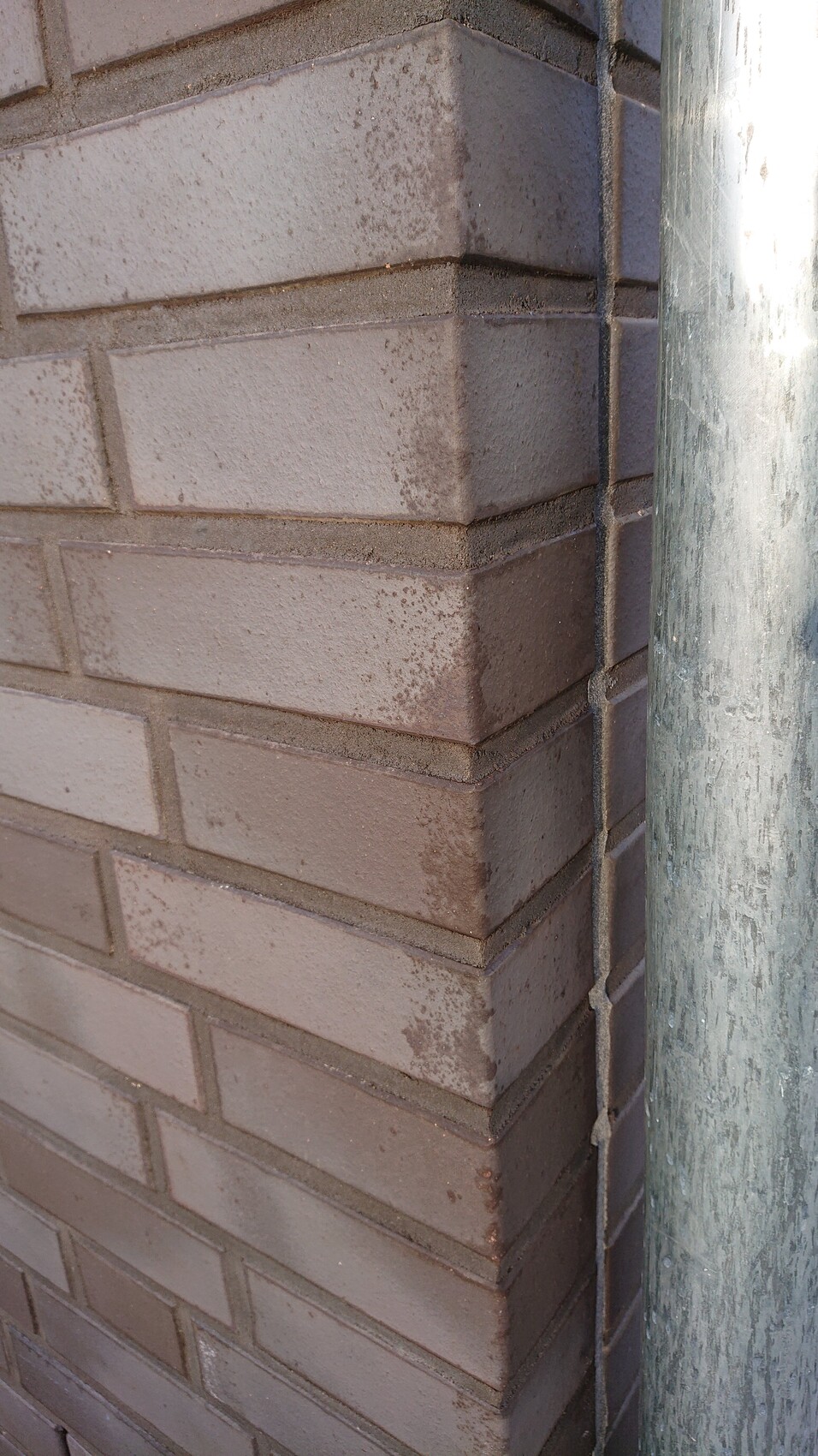 Eckansicht einer braunen Backsteinwand mit senkrechtem Metallrohr.
