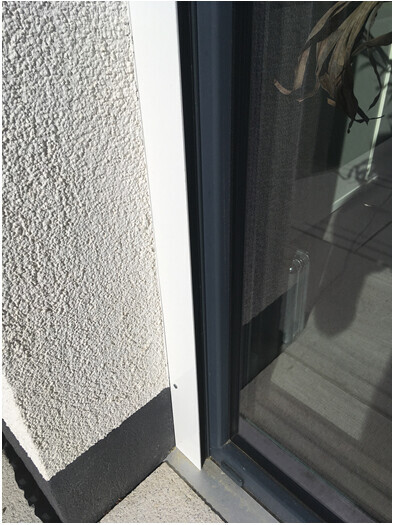 Nahaufnahme eines Fensterrahmens neben rauer Wandputzstruktur.