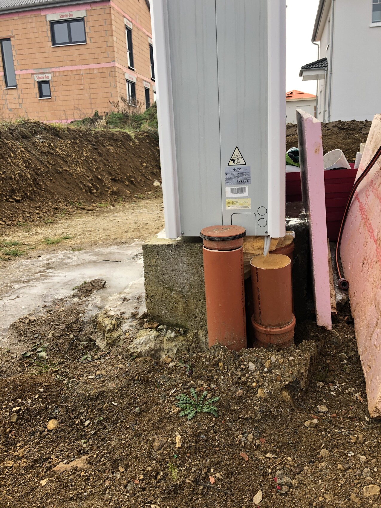 Baustelle: großer Schaltschrank auf Fundament, davor braune Rohre und pinke Dämmplatten.