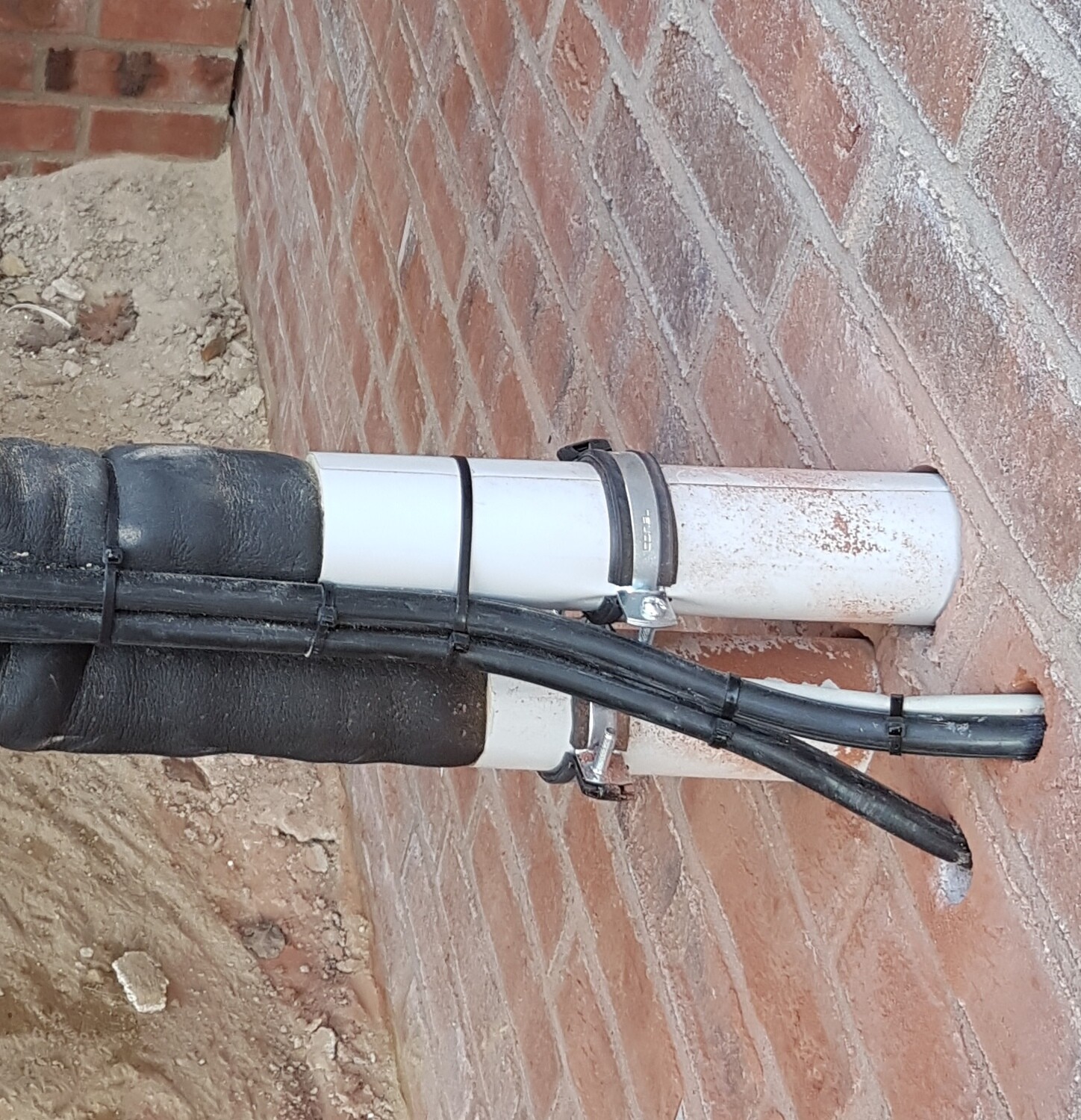 PVC-Rohrleitung an einer Ziegelwand mit Metallklemme und schwarzen Kabeln