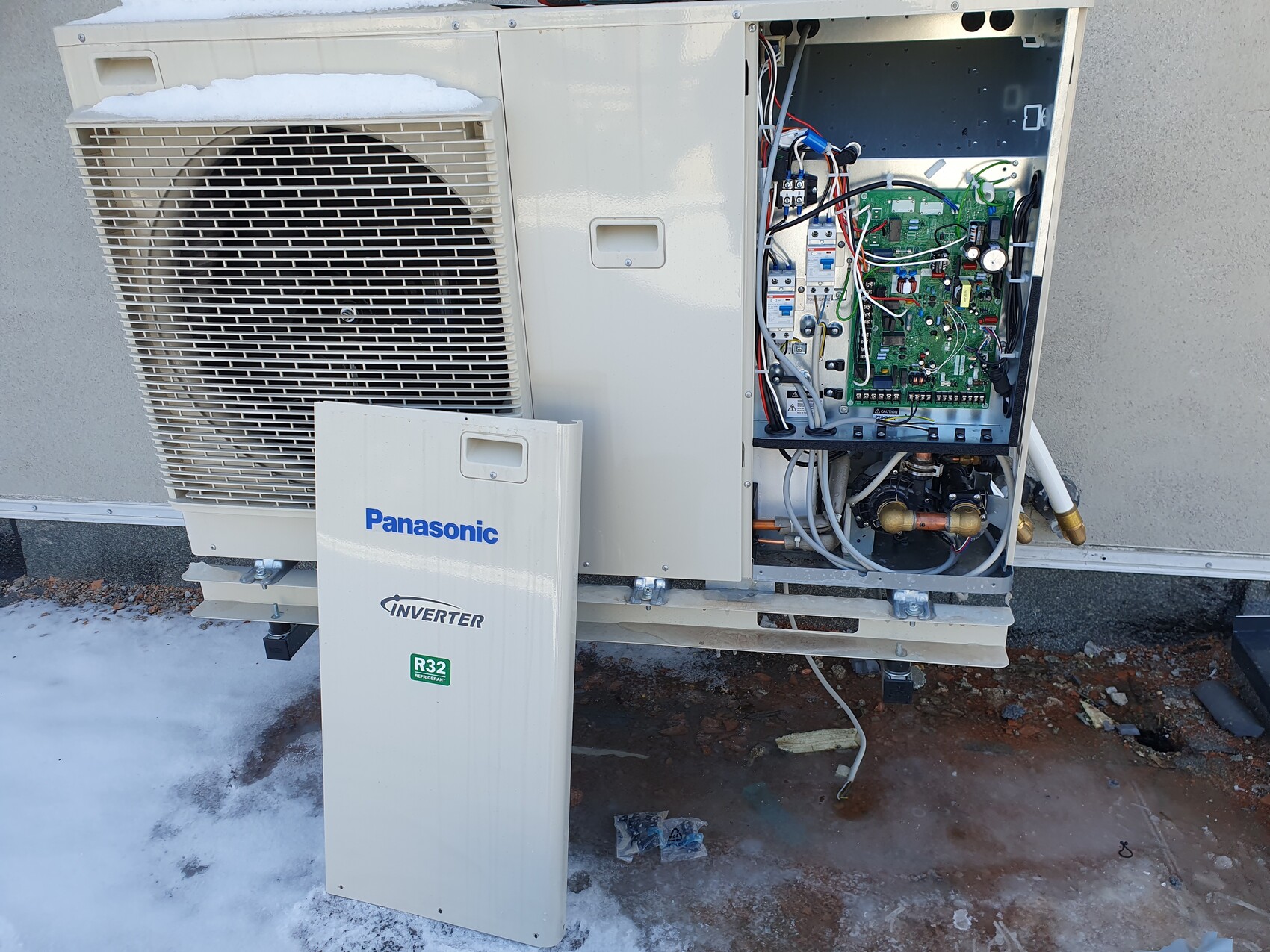 Außenmodul einer Panasonic Inverter-Klimaanlage mit offenem Elektronikpanel, Rohren; Schnee.