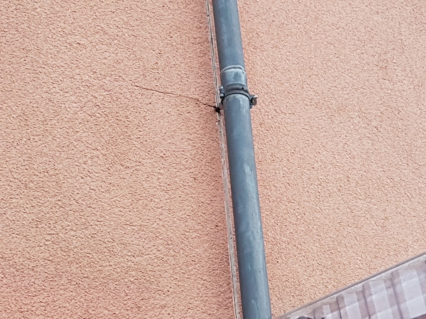 Graues Außenrohr an orange gestrichener Hauswand, Teil der Haustechnik.