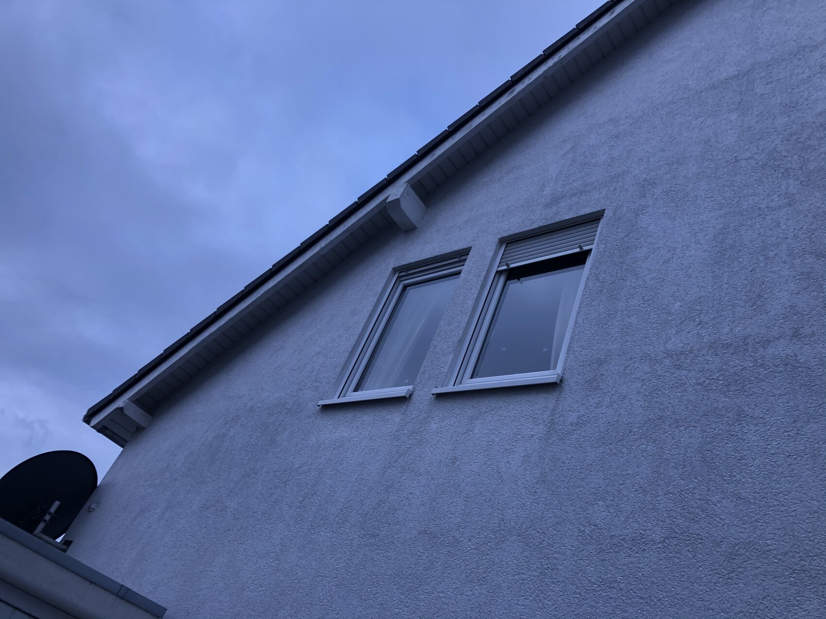 Außenfassade eines Hauses mit zwei Fenstern unter dem Dach, bläulich gefärbter Himmel.