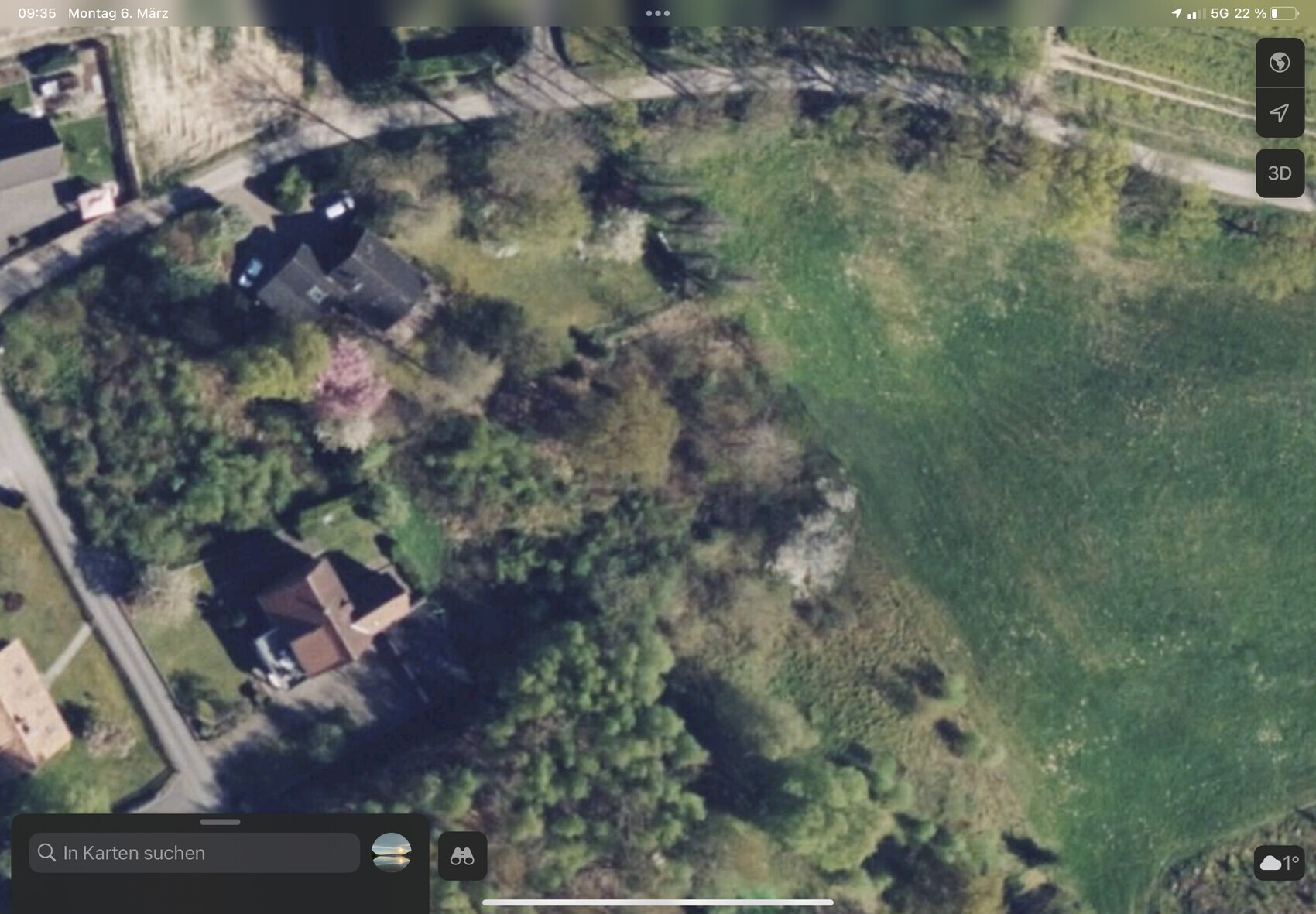 Luftbild eines Grundstücks mit Haus, Garten und dichter Bepflanzung an einer Straße.