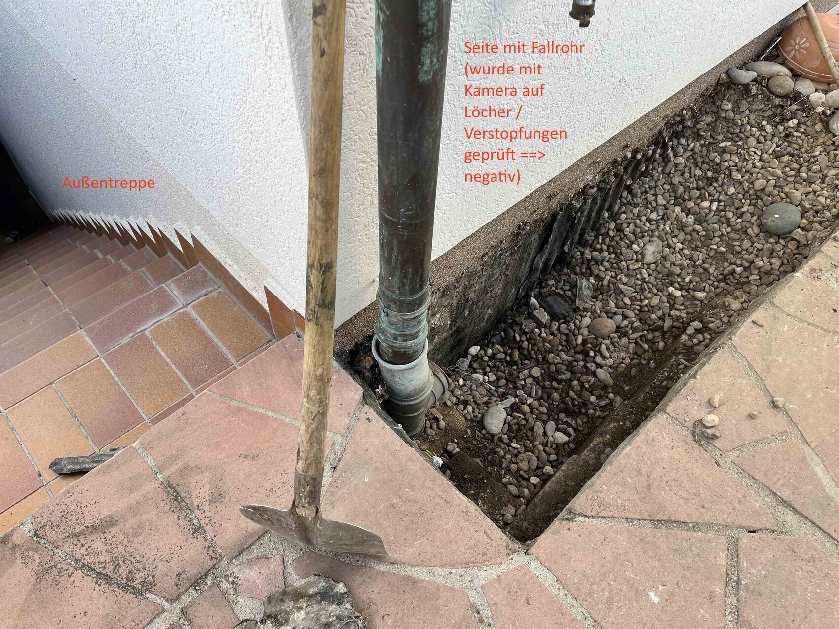 Außentreppe links, Fallrohr am Mauerwerk, Graben mit Kies und Spaten davor