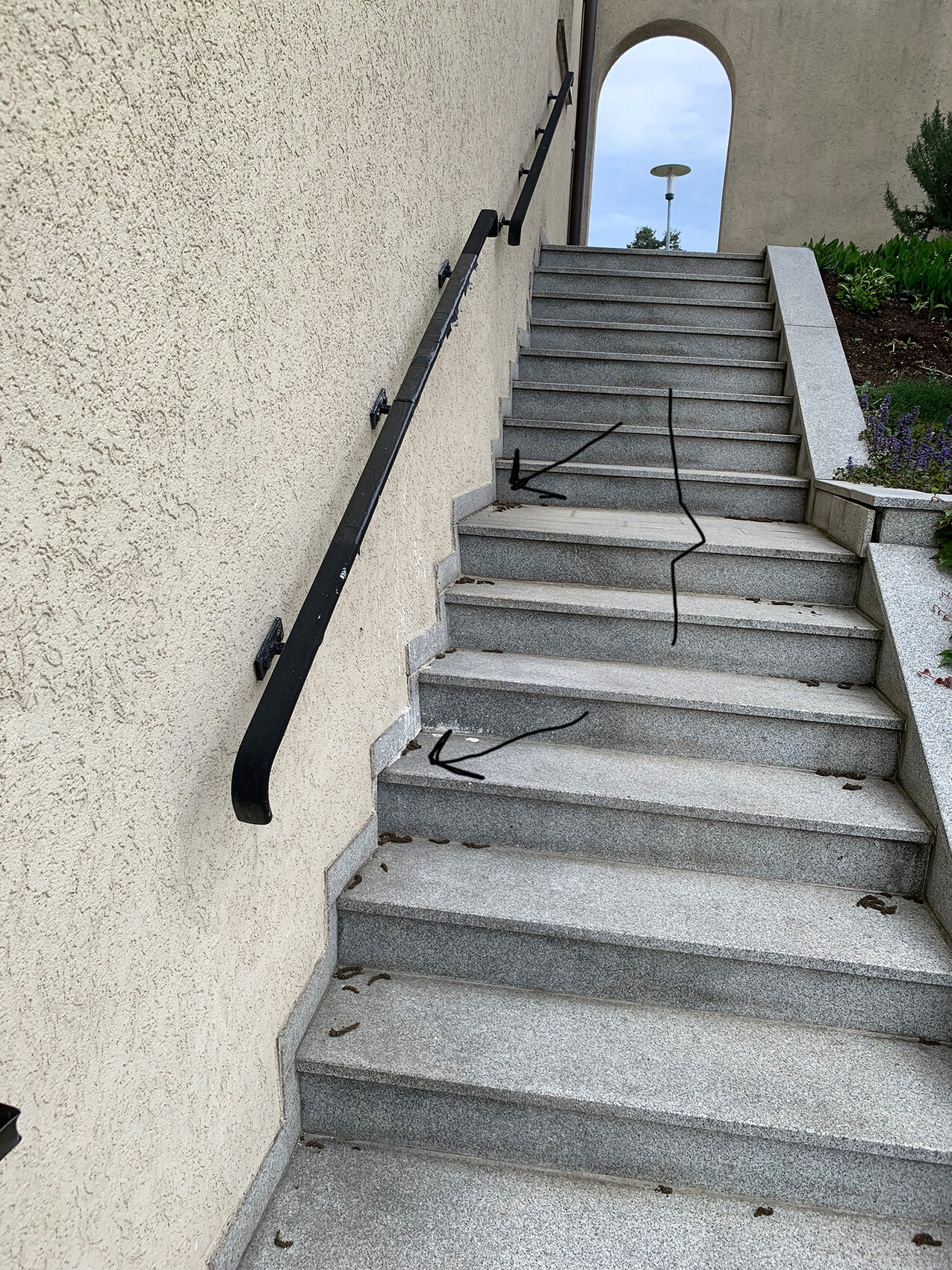 Außentreppe mit grauen Stufen und schwarzem Handlauf neben beige verputzter Wand