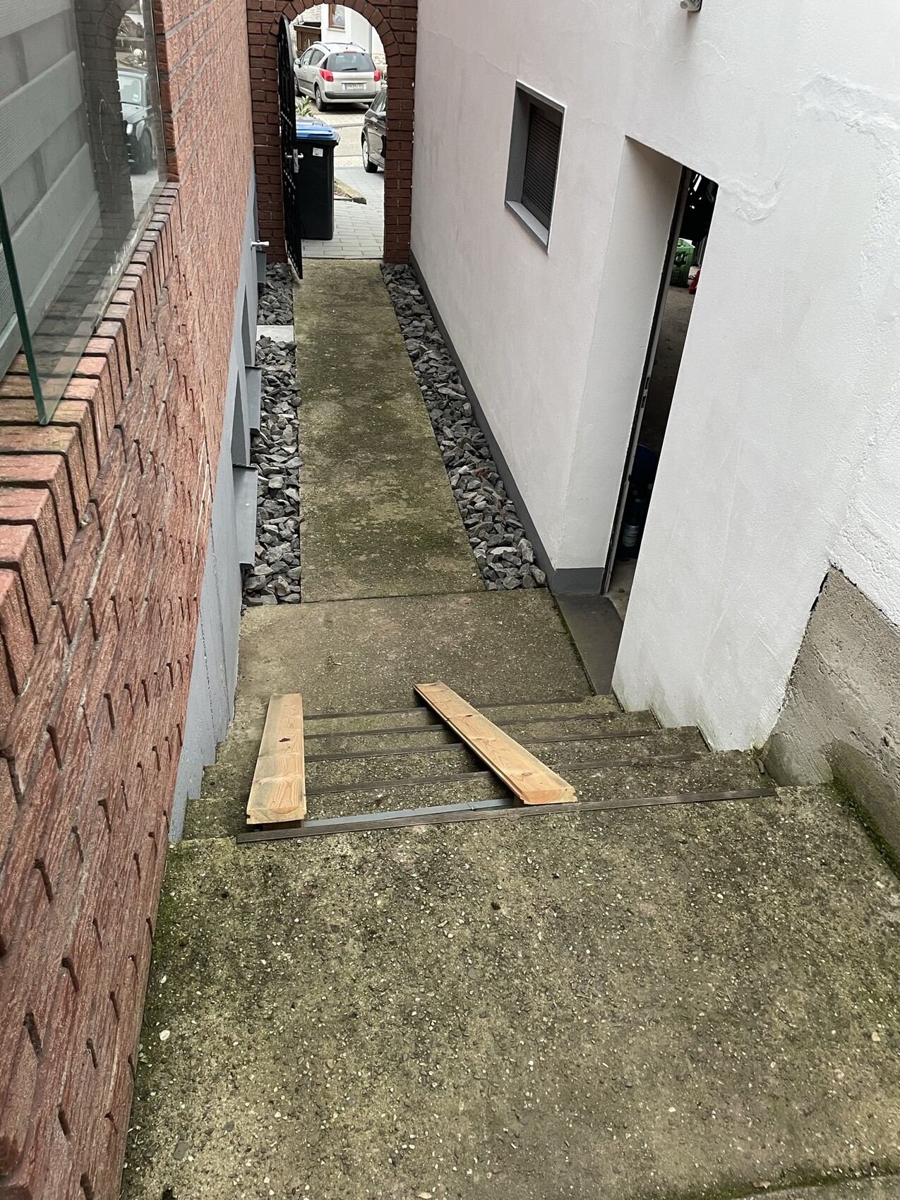 Enge Treppe zwischen rotem Backstein links und weißer Wand rechts; Holzbretter liegen auf Stufen.