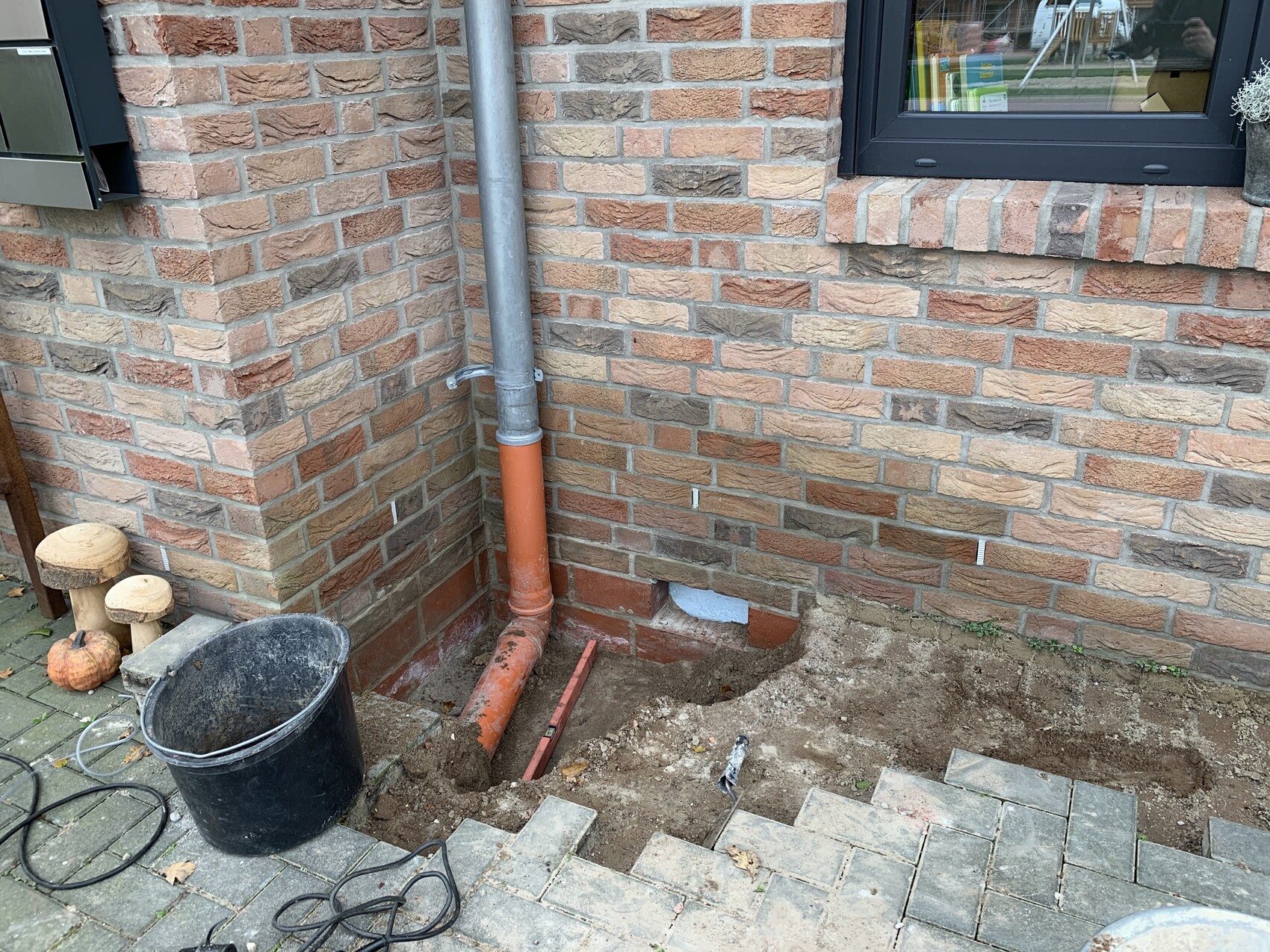 Außenwand aus Ziegeln mit grauem Regenrohr, orangefarbener Rohrleitung im Grab; Eimer und Werkzeuge