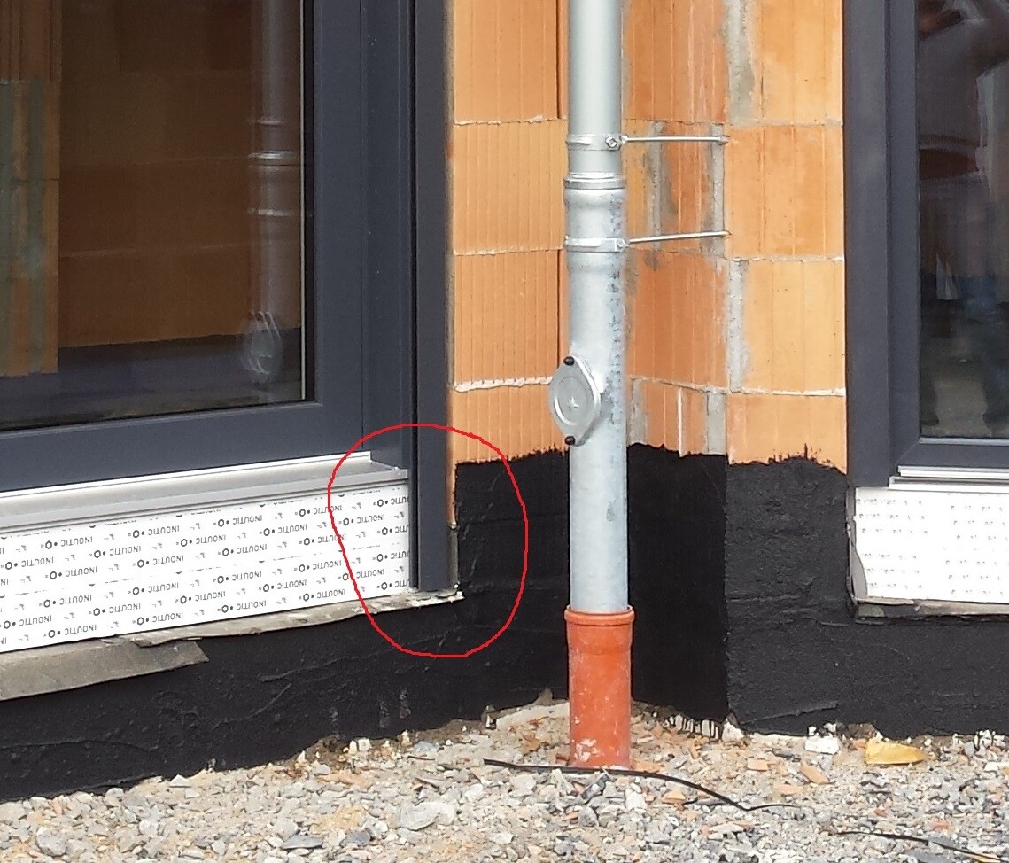 Außenwandbau mit Fensterrahmen, Regenrinne und schwarzer Abdichtung am Fundament