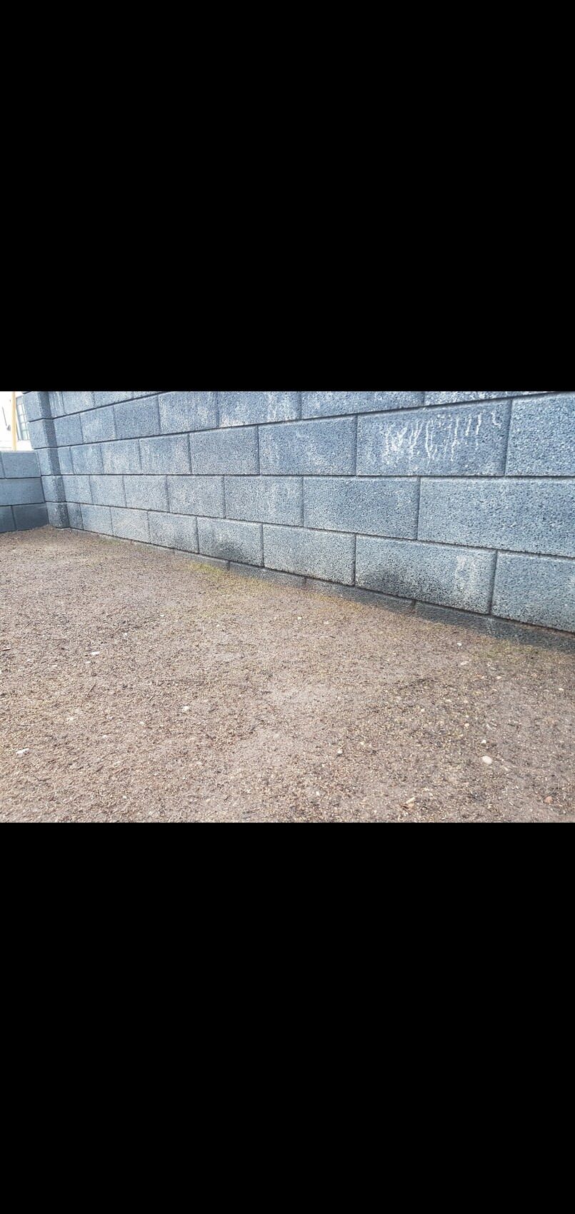 Graue Betonblockwand am Bauplatz mit unbefestigtem Boden