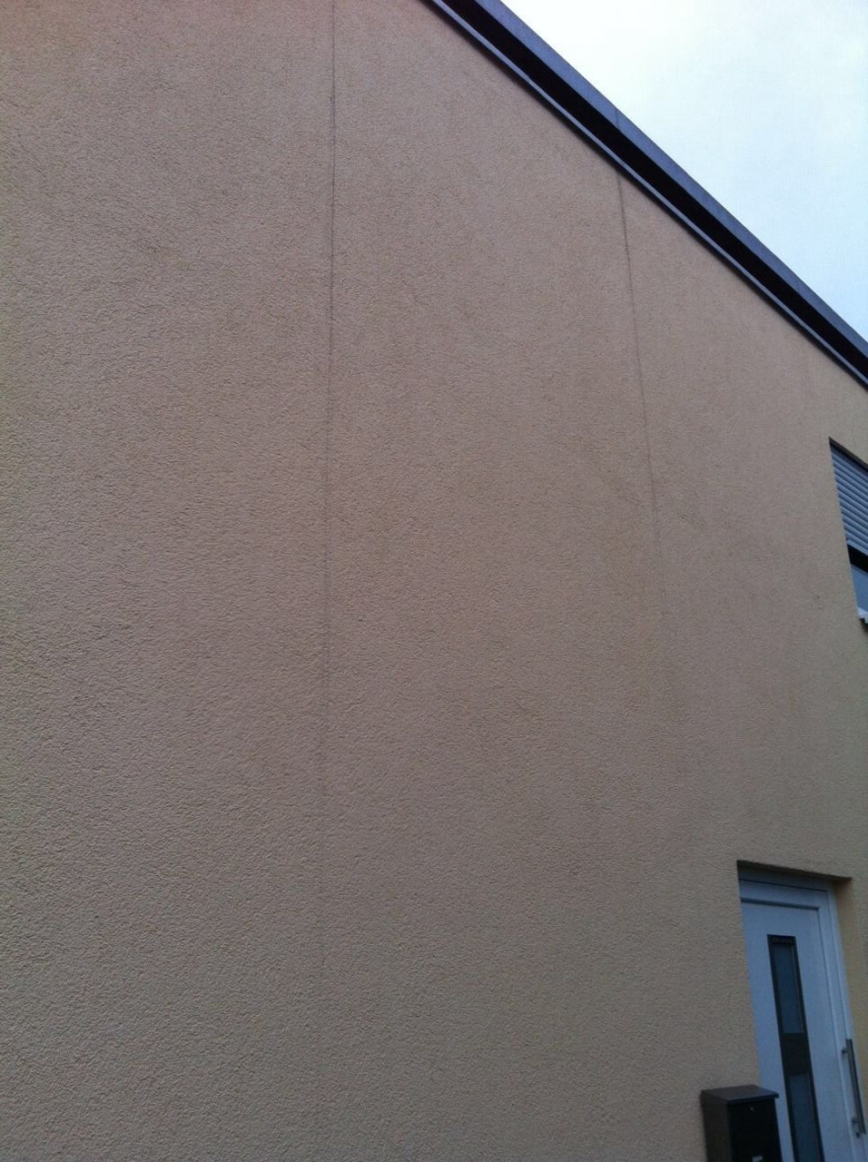 Grobe Aufnahme einer beigefarbenen Außenfassade mit Tür unten rechts.